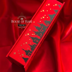 K&ouml;nnte beinhalten: Eine rote Schachtel mit einem schwarzen Silhouette-Design einer Stadtlandschaft und goldenen Sternen. Auf der Schachtel steht "HOUSE OF FLARE" und "ANDRE CARR". Die Schachtel liegt auf einer roten Satin-Oberfl&auml;che.