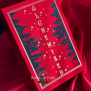 K&ouml;nnte beinhalten: Ein rotes Buch mit goldenem Rand und dem Titel "ALCHEMISED" in Wei&szlig;. Das Cover zeigt ein dunkelblaues Silhouette-Design von Geb&auml;uden und Sternen. Das Buch liegt auf einem roten Satinhintergrund, mit dem Logo "HOUSE OF FLARE" sichtbar.