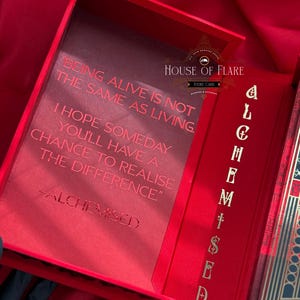 K&ouml;nnte beinhalten: Ge&ouml;ffnete rote Box mit goldfarbenen Buchstaben und dem Text "BEING ALIVE IS NOT THE SAME AS LIVING." Die Box hat auch den Text "ALCHEMISED" und "HOUSE OF FLARE". Die Box ist ge&ouml;ffnet und zeigt einen roten Innenraum.