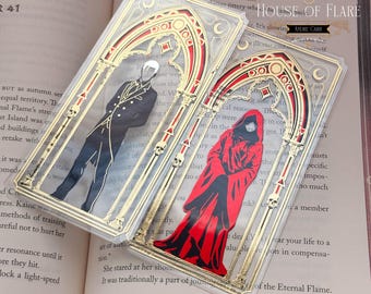 May include: Two rectangular clear acrylic bookmarks featuring gold foil gothic arch frames with skull accents. One bookmark displays a figure in a black suit, the other a figure in a red hooded cloak. Both include the text HOUSE OF FLARE ANDRE CARR.