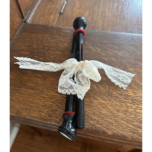 May include: Two black wooden curtain tiebacks with red accents and a cream-colored lace bow. The tiebacks have a rounded top and bottom, and are tied together with a delicate lace ribbon. The overall aesthetic is vintage and decorative.