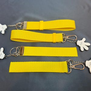 May include: Four yellow keychains with white cartoon hands attached. Each keychain has a silver ring and a silver clasp.