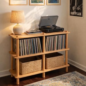 May include: A light wood record player stand with a black turntable, a tan lamp, and two woven baskets. The stand has three shelves filled with vinyl records. A Bob Dylan poster hangs on the wall.