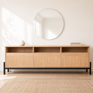 May include: A light oak wood media console featuring three open top shelves and three lower cabinets with solid doors, supported by a black metal frame. A large circular mirror with a thin frame is mounted on the wall above the console.