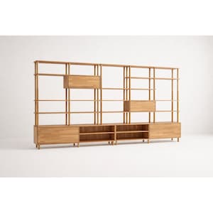 May include: A large, light-colored wooden shelving unit with multiple open shelves, drawers, and cabinets. The unit is constructed with vertical supports and horizontal shelves, offering ample storage space. The design is minimalist and modern, suitable for various home decor styles.