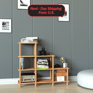 May include: A wooden shelf unit with five shelves, featuring a camera, books, and a radio. The shelf unit is made of natural wood and has a simple, modern design.