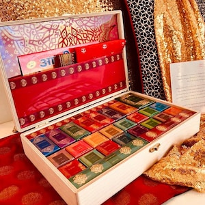 May include: A wooden box with a hinged lid, filled with colorful, small, book-shaped items. The box is lined with red fabric and gold accents. The background includes red and gold textiles.