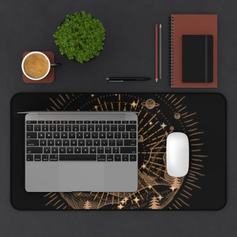 May include: A black and gold desk mat with a celestial design featuring stars, planets, and a crescent moon. The mat is surrounded by a gold border and has a subtle shimmer.