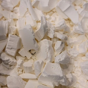 May include: Close-up of a pile of irregularly shaped, off-white chunks. The pieces vary in size and texture, with some appearing smooth and others rough. The overall impression is of a dense, solid material.
