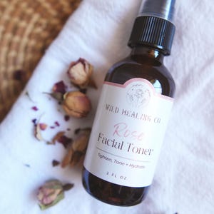 May include: A brown glass bottle with a black spray nozzle and a white label that reads "WILD HEALING CO Rose Facial Toner Tighten, Tone + Hydrate 2 FL OZ".
