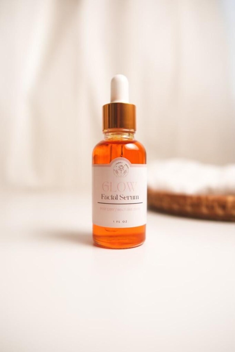K&ouml;nnte beinhalten: Eine Glasflasche mit Gesichts-Serum mit goldenem Deckel und Tropfer. Die Flasche ist mit "Glow Facial Serum" beschriftet und enth&auml;lt eine klare orange Fl&uuml;ssigkeit. Die Flasche steht auf einer wei&szlig;en Oberfl&auml;che.