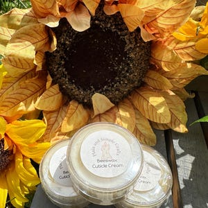 May include: Three small, clear, round plastic containers filled with off-white beeswax cuticle cream. Each lid features a circular white label with the text "Plain and Simple Crafts" and "Beeswax Cuticle Cream" surrounding a candle icon.