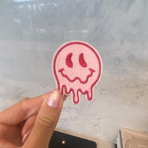 Pode incluir: Patch bordado de ferro rosa e vermelho com um rosto sorridente derretido.