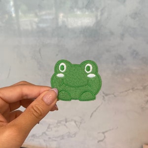 May include: Green felt frog patch with white embroidered eyes and a smile.