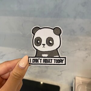 Pode incluir: Um remendo de ferro bordado em branco e preto com um panda de desenho animado com o texto "Não posso ser adulto hoje".