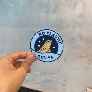 May include: A blue and black round patch with the text "NO PLASTIC OCEAN" and a cartoon image of a bird.