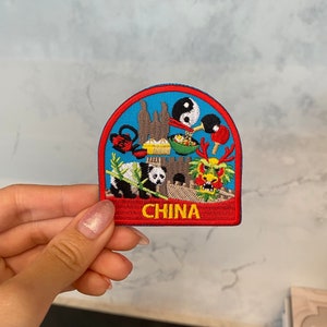 May include: An embroidered iron-on patch featuring a colourful design of iconic Chinese symbols, including a panda, dragon, pagoda, and yin-yang symbol. The patch has a red border with the word "CHINA" in yellow lettering.