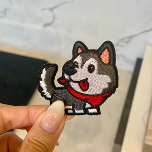 May include: Embroidered iron-on patch featuring a cartoon husky dog with a red bandana. The dog is gray and white with black eyes and a pink nose. The patch is approximately 2 inches tall.