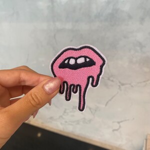 Peut inclure: Patch brodé rose à repasser d'une bouche qui coule et fond avec des dents blanches.