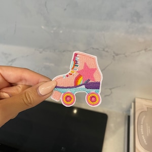 Op de afbeelding: Roze geborduurde rolstoelpatch met een regenboog, ster en gele wielen.