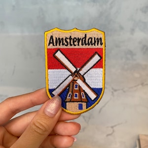 May include: A yellow, red, white, and blue embroidered patch with a windmill and the word "Amsterdam" on it.