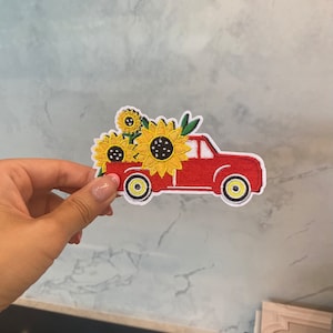 Könnte beinhalten: Roter LKW mit einer Ladefläche voller gelber Sonnenblumen. Der LKW hat weiße Räder und einen weißen Umriss. Der Patch ist gestickt.