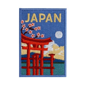 Peut inclure: Écusson brodé représentant un paysage japonais. Le motif comprend un torii rouge, des fleurs de cerisier, une pleine lune et le mot "JAPAN" en lettres dorées sur fond bleu. L'écusson a une bordure bleue.