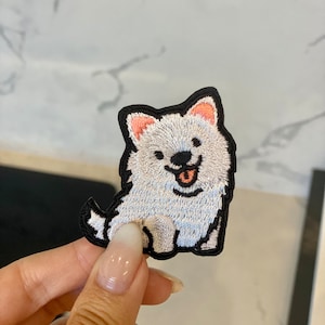 Op de afbeelding: Witte geborduurde strijkpatch van een cartoonhond met zwarte ogen, een roze neus en een zwarte omtrek.