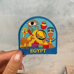 May include: A blue and yellow embroidered patch with Egyptian symbols, including an eye, a pyramid, a camel, and the word "EGYPT".