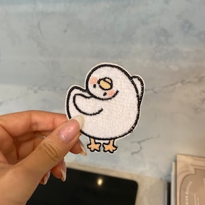 May include: White embroidered iron-on patch of a cartoon chick with black eyes and a pink blush. The chick is standing on two legs with orange feet.