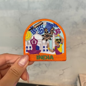 Puede incluir: Un parche bordado naranja y azul con una imagen del Taj Mahal, una persona haciendo yoga, una persona sosteniendo un plato de comida y un bate de cricket. El parche tiene la palabra "INDIA" escrita en él.