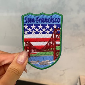 May include: A blue and green embroidered patch with the text "San Francisco" and an image of the Golden Gate Bridge with the American flag in the background.