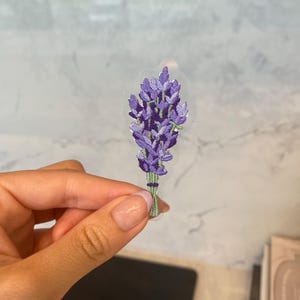 May include: An embroidered lavender flower patch in purple and green. The patch is on a clear background.
