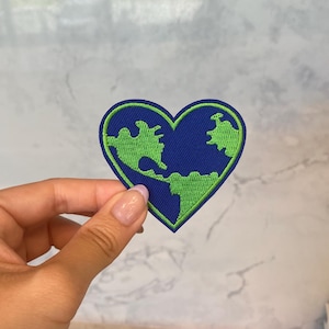 May include: A green and blue embroidered patch shaped like a heart with a stylised image of the Earth inside.