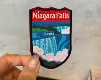 Op de afbeelding: Een geborduurde patch met een afbeelding van Niagara Falls en de tekst "Niagara Falls". De patch is rood, zwart en blauw.