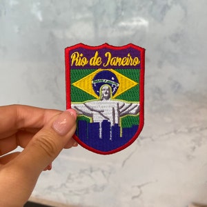 Puede incluir: Parche bordado con la inscripción "Rio de Janeiro". El parche muestra la bandera brasileña y la estatua del Cristo Redentor. El parche es rojo, verde, azul y morado. Ideal para chaquetas o bolsos.