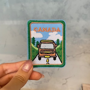 May include: A blue and green embroidered patch featuring a yellow and orange cartoon bus driving on a white road with the word "CANADA" in orange letters.
