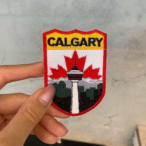 May include: Red, white, and yellow embroidered patch with the word "CALGARY" in black lettering. The patch features a red maple leaf with a white tower in the center, and a green and black cityscape below.
