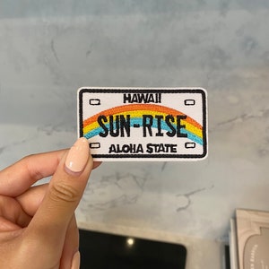 Könnte beinhalten: Weißer gestickter Patch mit einem Regenbogen-Design und dem Text "HAWAII SUN-RISE ALOHA STATE".