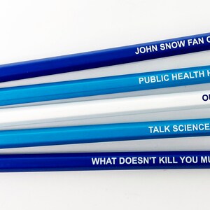 May include: Five blue pencils with white lettering. The pencils have the following text: "JOHN SNOW FAN CLUB", "PUBLIC HEALTH HERO", "OUTLIER", "TALK SCIENCE TO ME", and "WHAT DOESN'T KILL YOU MUTATES".