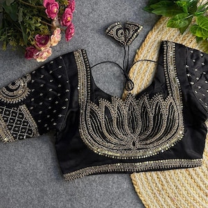 May include: Black blouse with gold embellishments. The blouse features a lotus flower design on the front, with intricate beadwork and sequin detailing. The sleeves and neckline are also adorned with gold accents. The blouse is a formal wear item.