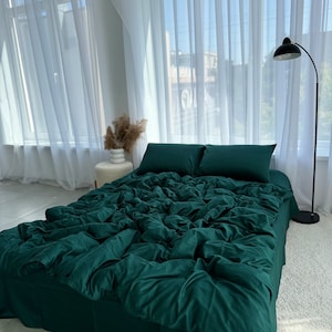 Könnte beinhalten: Ein tiefgrünes Bettwäsche-Set aus Leinen mit einem Bettbezug, zwei Kissenbezügen und einem Spannbettlaken. Die Bettwäsche ist auf einem Bett mit einem weißen Kopfteil und einem weißen Teppich angeordnet.