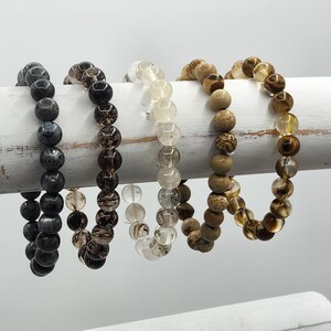 May include: Four beaded bracelets in different colors and patterns. The bracelets are made of black, brown, clear, and light brown beads.