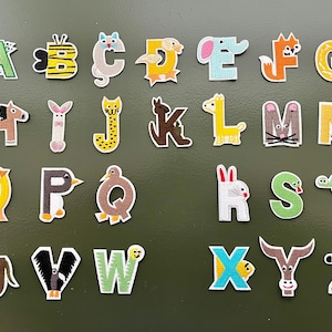 May include: A set of 26 iron-on patches featuring the alphabet in a whimsical style. Each letter is decorated with a different animal design, such as a bee, cat, elephant, fox, and zebra. The patches are perfect for adding a touch of personality to clothing, bags, or other fabric items.