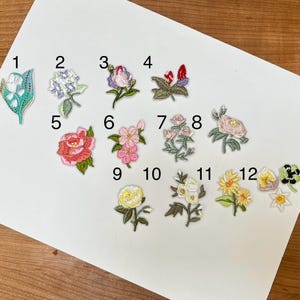May include: A collection of twelve embroidered floral patches in various colors. The patches include designs of roses, lilies, and other flowers. Each patch is intricately detailed with different colors and textures, perfect for adding to clothing or accessories.