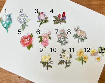 May include: A collection of twelve embroidered floral patches in various colors. The patches include designs of roses, lilies, and other flowers. Each patch is intricately detailed with different colors and textures, perfect for adding to clothing or accessories.