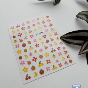 May include: A sheet of colorful stickers with various fruit and flower designs. The stickers are on a white background and feature cherries, bananas, oranges, and flowers in shades of yellow, orange, pink, and red. The text "JO-2018" is printed in the center of the sheet.