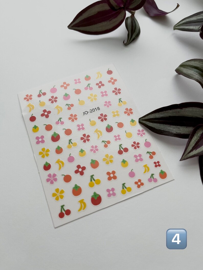 May include: A sheet of colorful stickers with various fruit and flower designs. The stickers are on a white background and feature cherries, bananas, oranges, and flowers in shades of yellow, orange, pink, and red. The text "JO-2018" is printed in the center of the sheet.