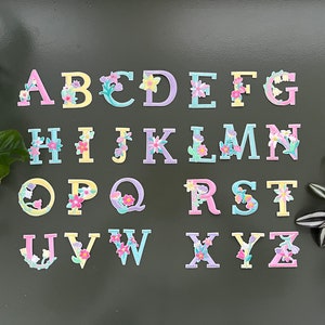 May include: A colorful alphabet with floral accents. Each letter is decorated with pink, yellow, and blue flowers. The letters are arranged in alphabetical order.