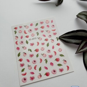 May include: A sheet of peach-themed nail stickers with pink peaches, green leaves, and pink flower petals. The sheet is labeled "JO-2012".